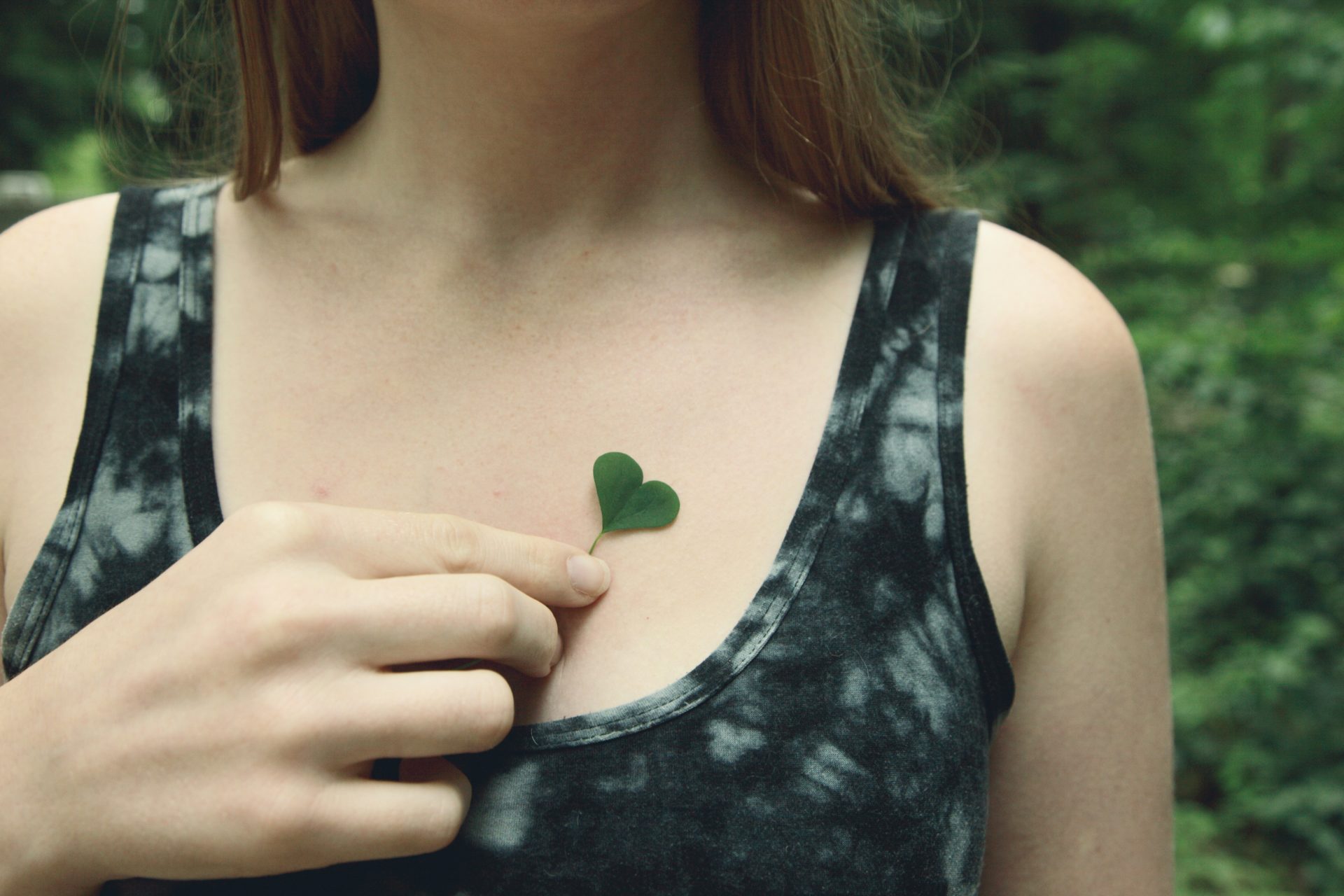 Eine Frau hält ein herzförmiges Blatt auf ihr Herz.