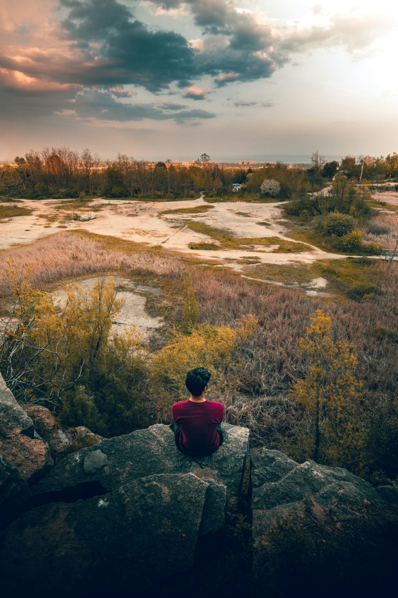 Ein Mann sitzt auf einem Felsen und schaut über eine weite Landschaft